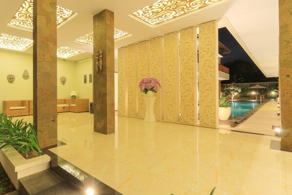 A well-lit lobby with a marble floor, a reception area with a sofa, and a view of an outdoor swimming pool at night. - Villa Linda 2 (Denpasar)