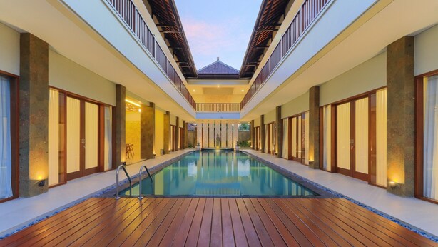 Una lunga e stretta piscina con bordo in legno, affiancata da pareti con ampie finestre e illuminazione calda.