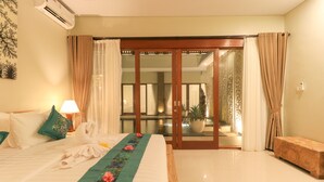 Una camera d'albergo con un letto, un comodino con una lampada, un bagno visibile tramite una porta in vetro e una pianta in vaso.