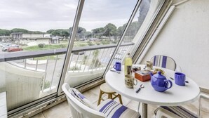 Un balcon avec une table et des chaises, une vue sur un parking et des immeubles, et un ciel dégagé.