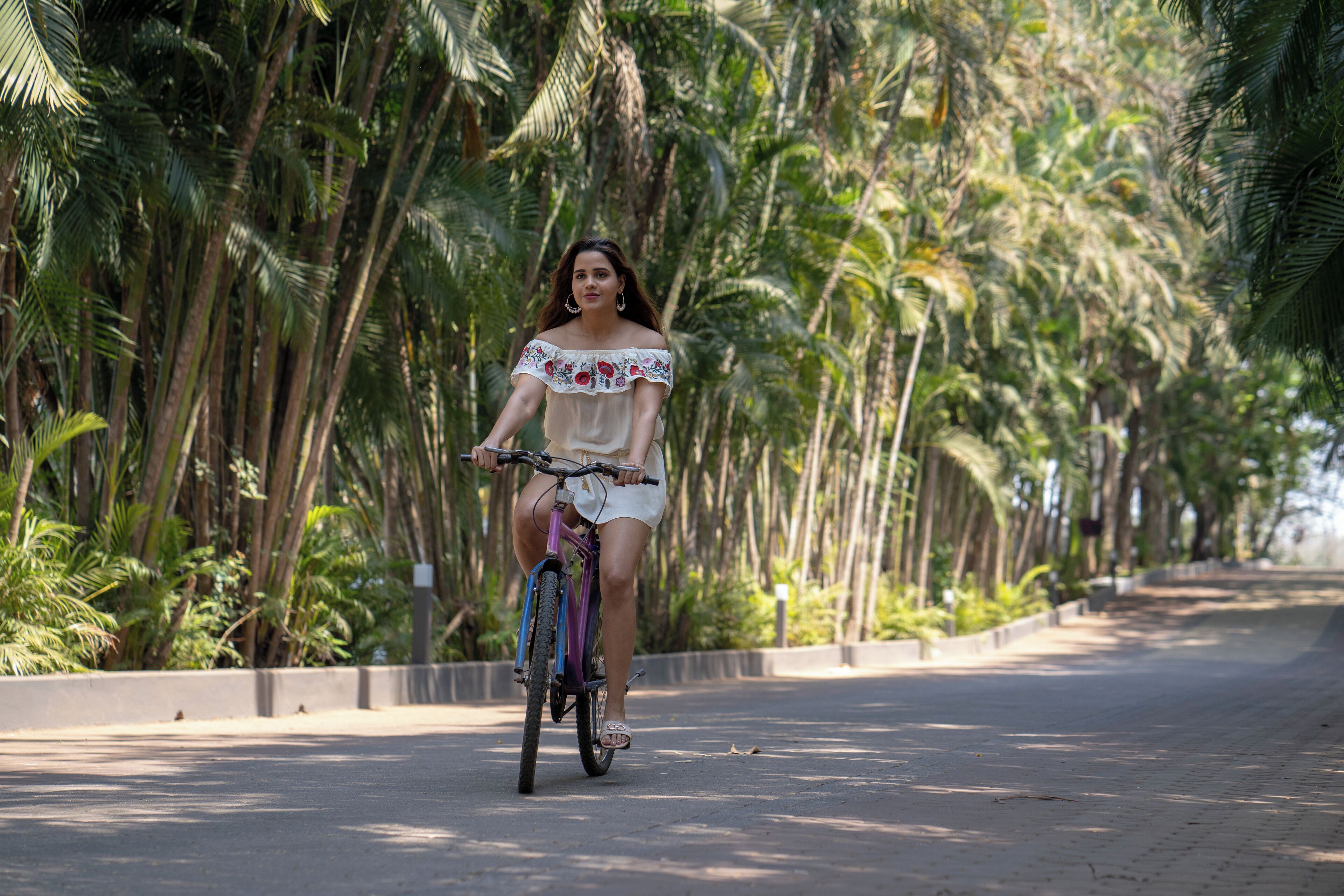 Una persona pedaleando en bicicleta por un camino pavimentado, rodeada de altas palmeras.