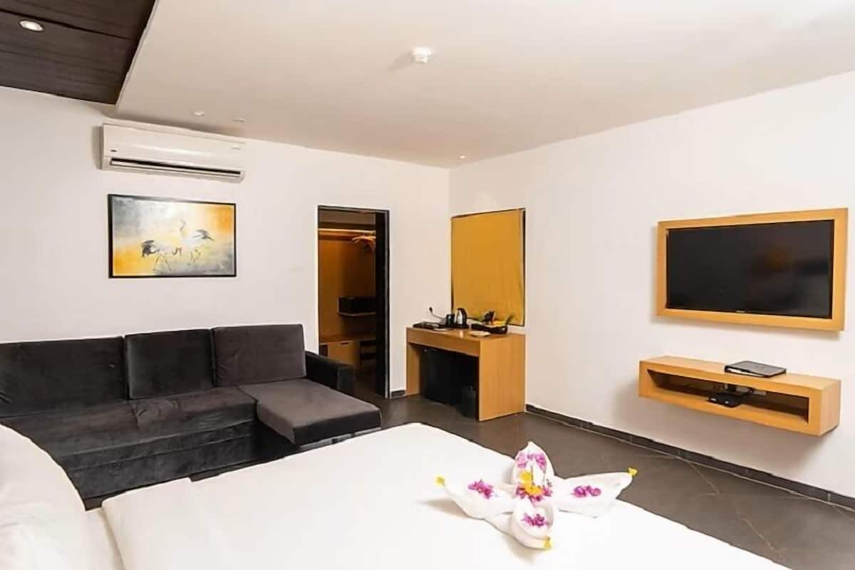 Una habitación de hotel moderna con cama, sofá, televisor, escritorio y armario.