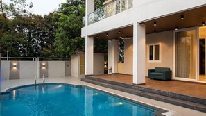 A modern outdoor pool area with a clear view of the pool, a covered seating area with a sofa, and a staircase leading to a second level. - U Rivergate Resort & Spa, Karjat (Karjat)