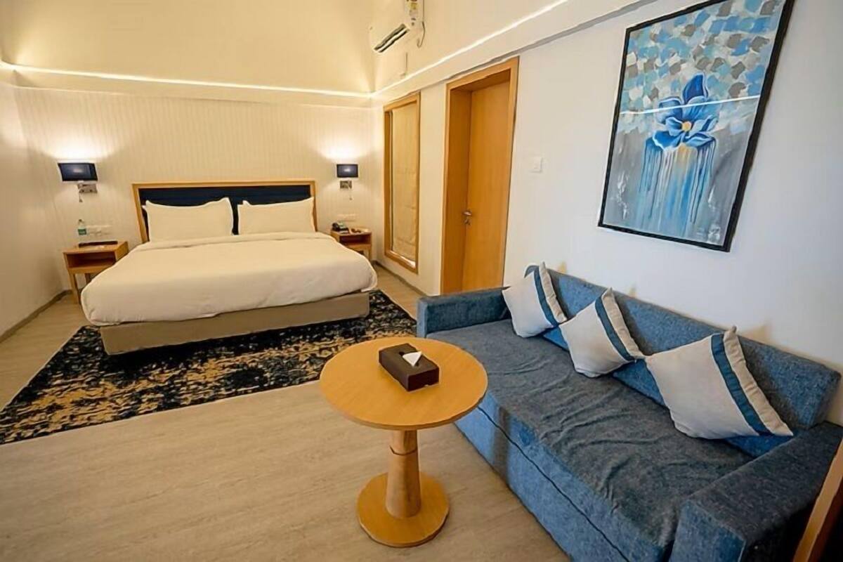 Habitación de hotel con cama, sofá, una mesita redonda y un cuadro en la pared.