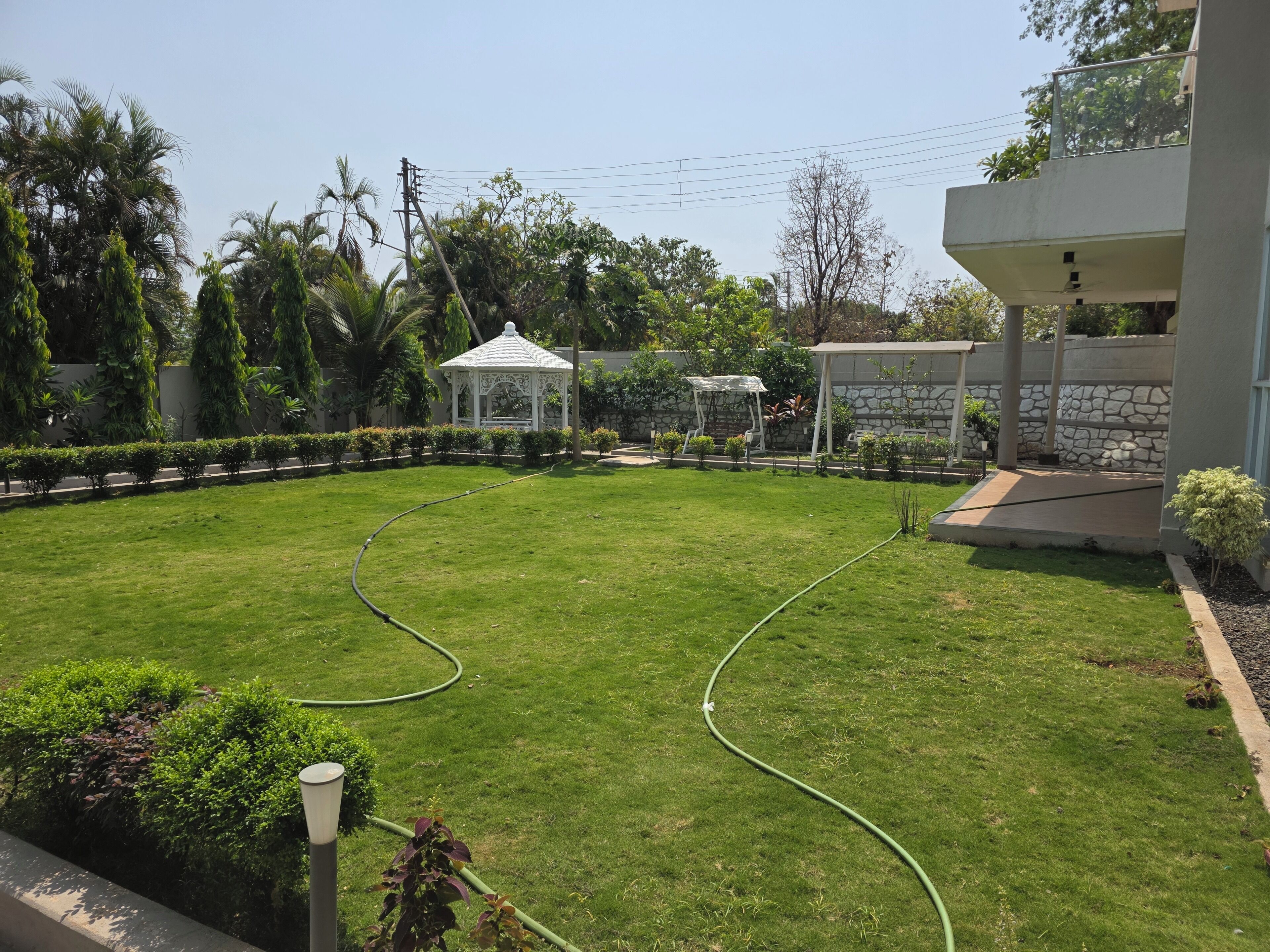 A well-maintained lawn with a gazebo, a stone wall, and a building with a balcony.