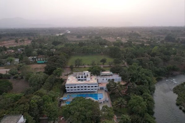 An aerial view of a building with a swimming pool, surrounded by greenery and a river. - U Rivergate Resort & Spa, Karjat (Karjat)