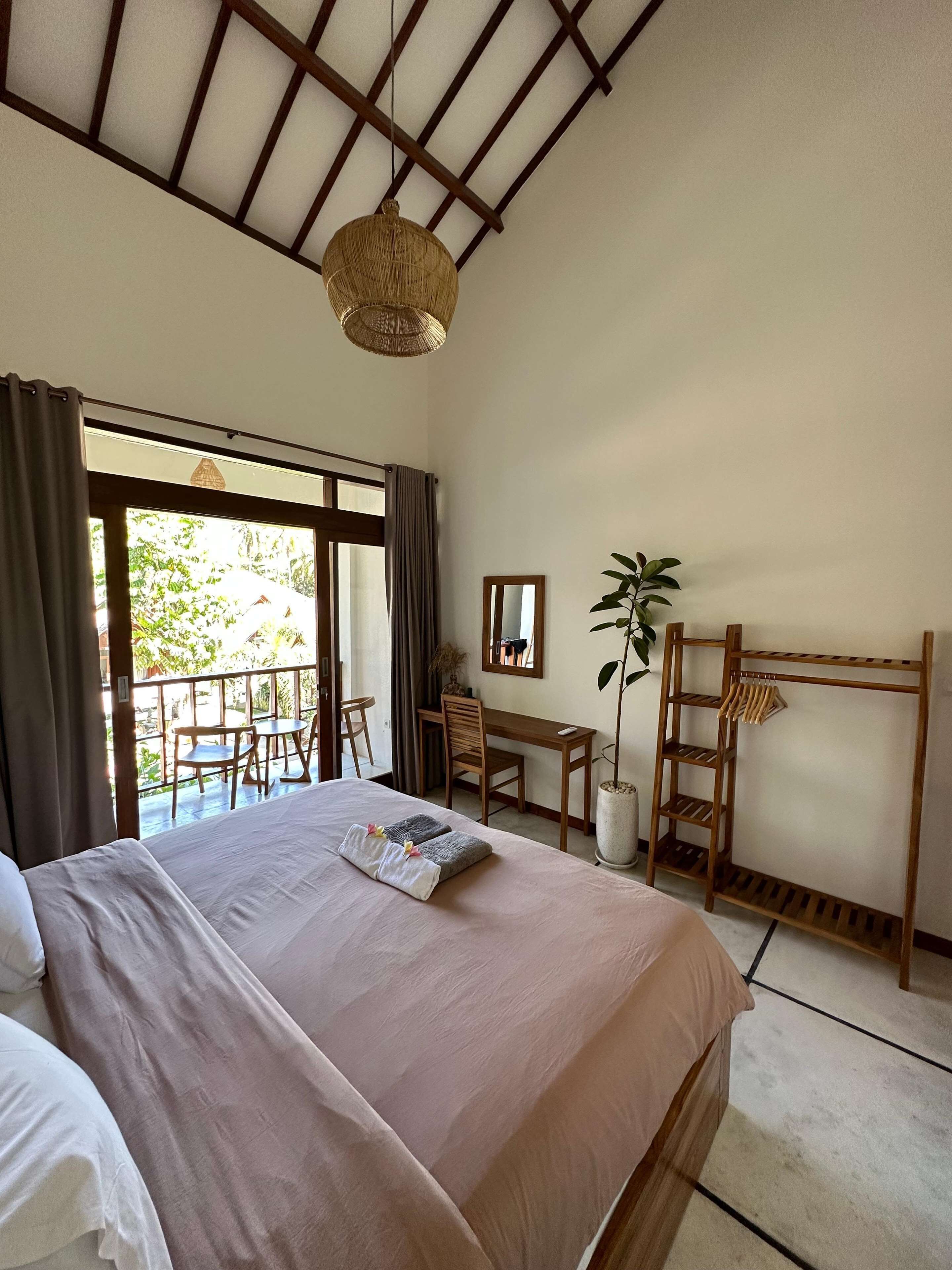 A bedroom with a large bed, a desk, a chair, a ladder, and a balcony with a view of greenery.