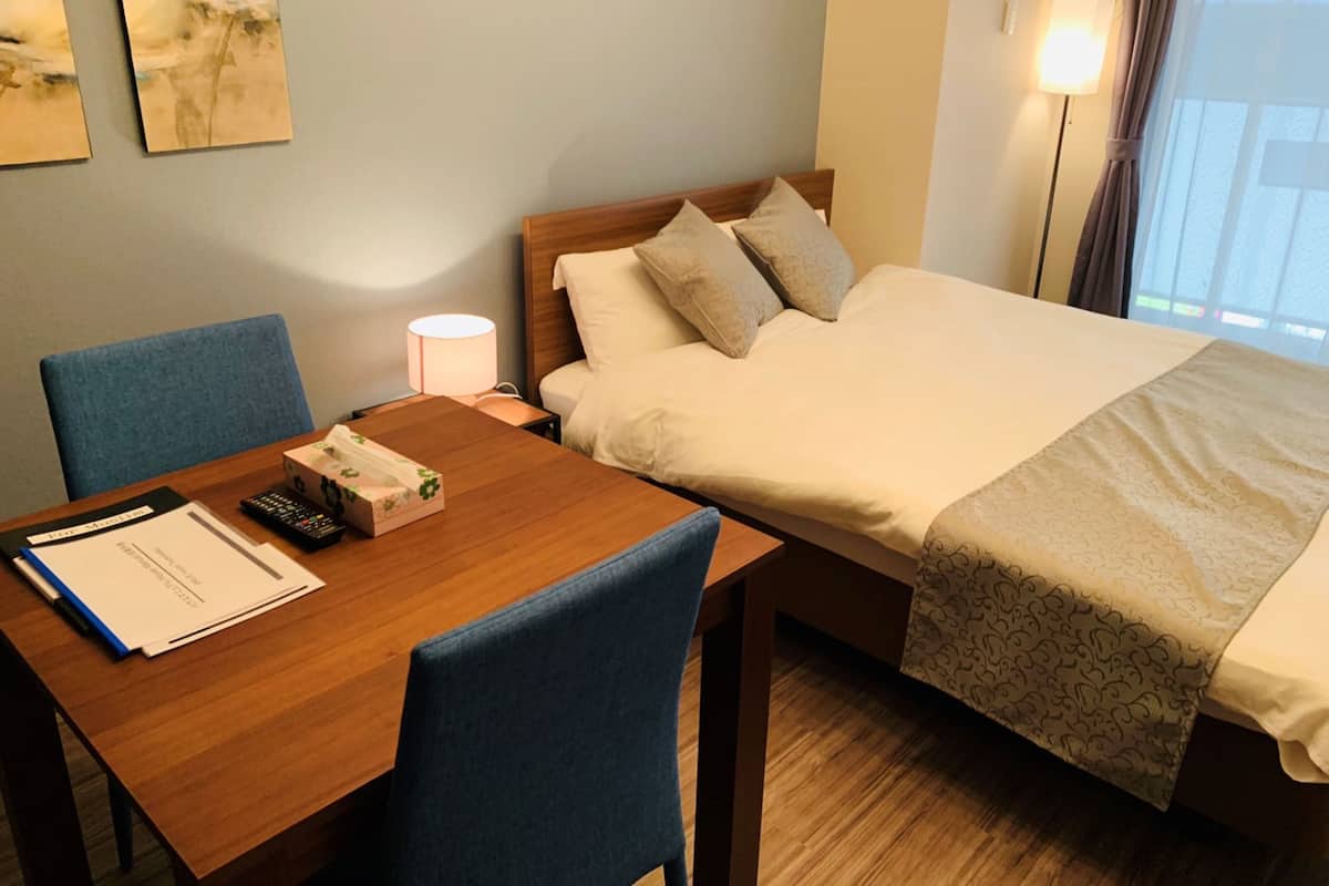 A hotel room with a bed, a desk with a chair, a nightstand with a lamp, and artwork on the wall.