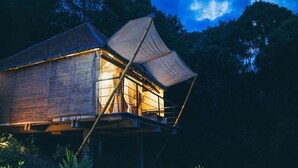 Eine Holzhütte mit einem großen Vordach, auf Stelzen stehend, umgeben von dichtem Wald.
