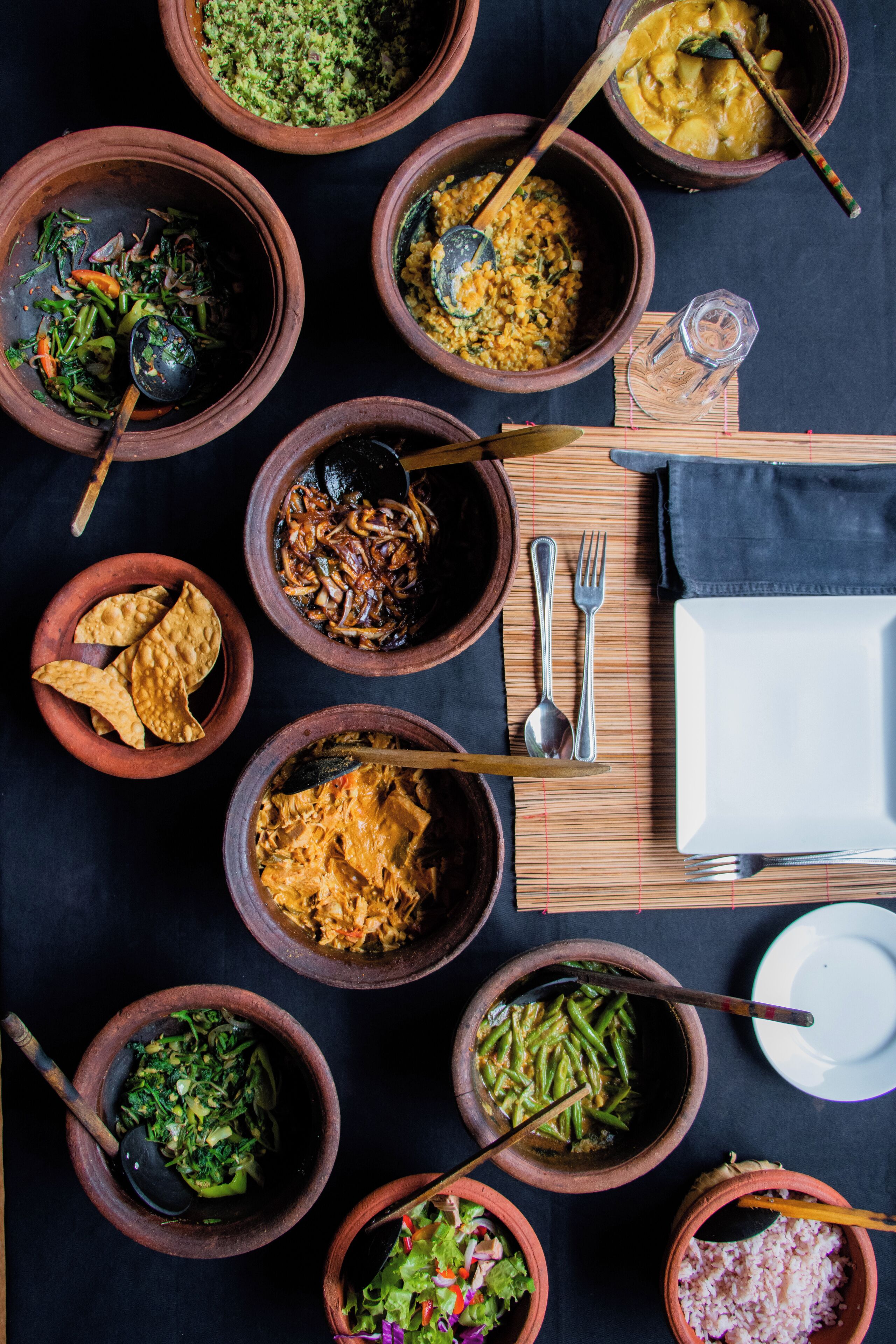 Una mesa dispuesta con diferentes platos en cuencos de barro, utensilios y un plato blanco.