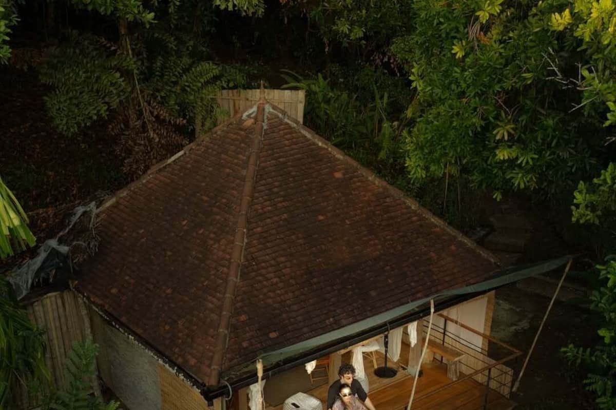 A small, single-story house with a tiled roof, surrounded by dense tropical foliage.
