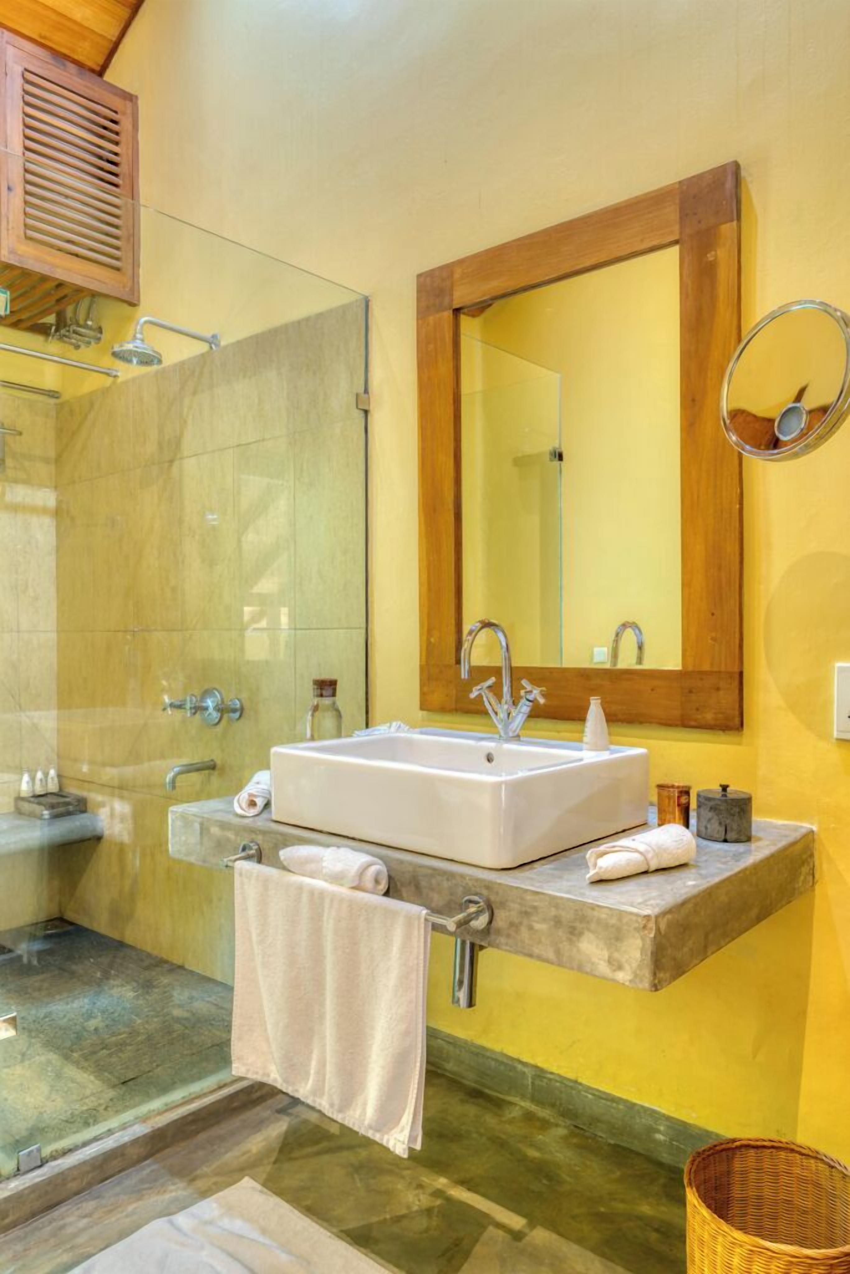 A bathroom with a glass shower enclosure, a white sink with a wooden countertop, and a large mirror with a wooden frame.