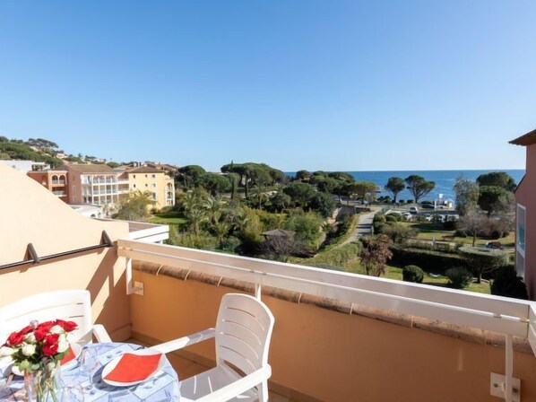 Un balcon avec une table et des chaises, donnant sur une zone côtière avec des bâtiments et des arbres.