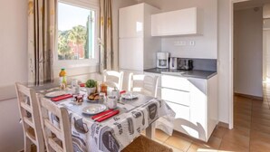A compact kitchen with white cabinets, a coffee maker, and a dining table set for two with chairs. - Les Rivages des Issambres by Interhome (Les Issambres)