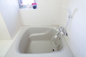 Ein Badezimmer mit Badewanne, einem Fenster mit Blumentöpfen und weißen Fliesenwänden.