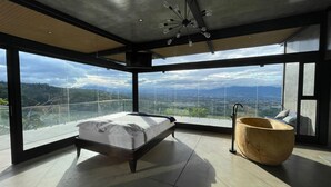 Een moderne slaapkamer met een groot bed, een houten bad en ruime ramen met uitzicht op de stad.