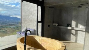 Een moderne badkamer met een groot houten bad, een douchegedeelte en uitzicht op het landschap door grote ramen.