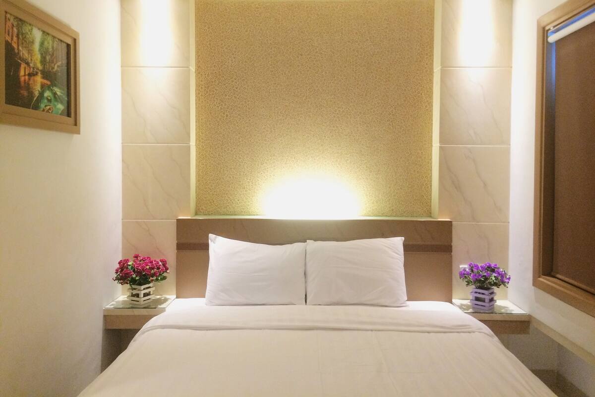 Una habitación de hotel con una cama, dos mesitas de noche, una lámpara de pared y un cuadro enmarcado.