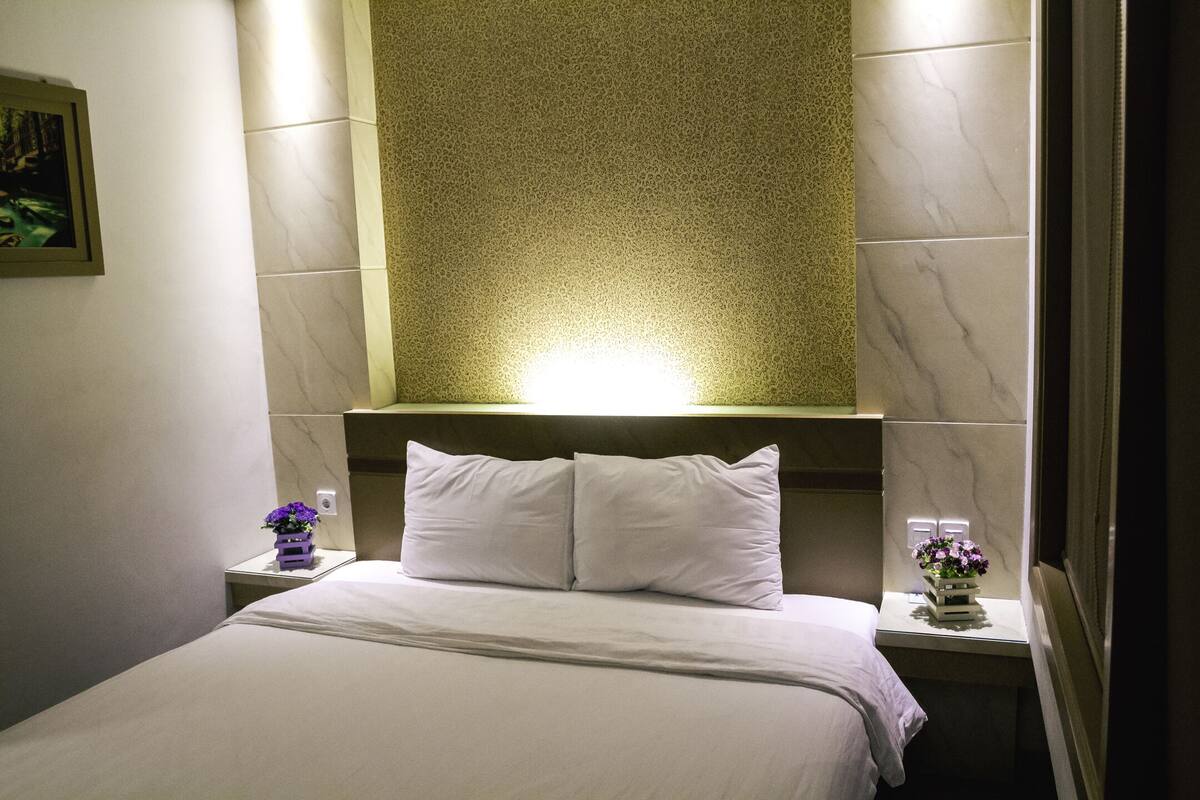 Habitación de hotel con cama, dos mesitas de noche y una lámpara fijada en la pared.