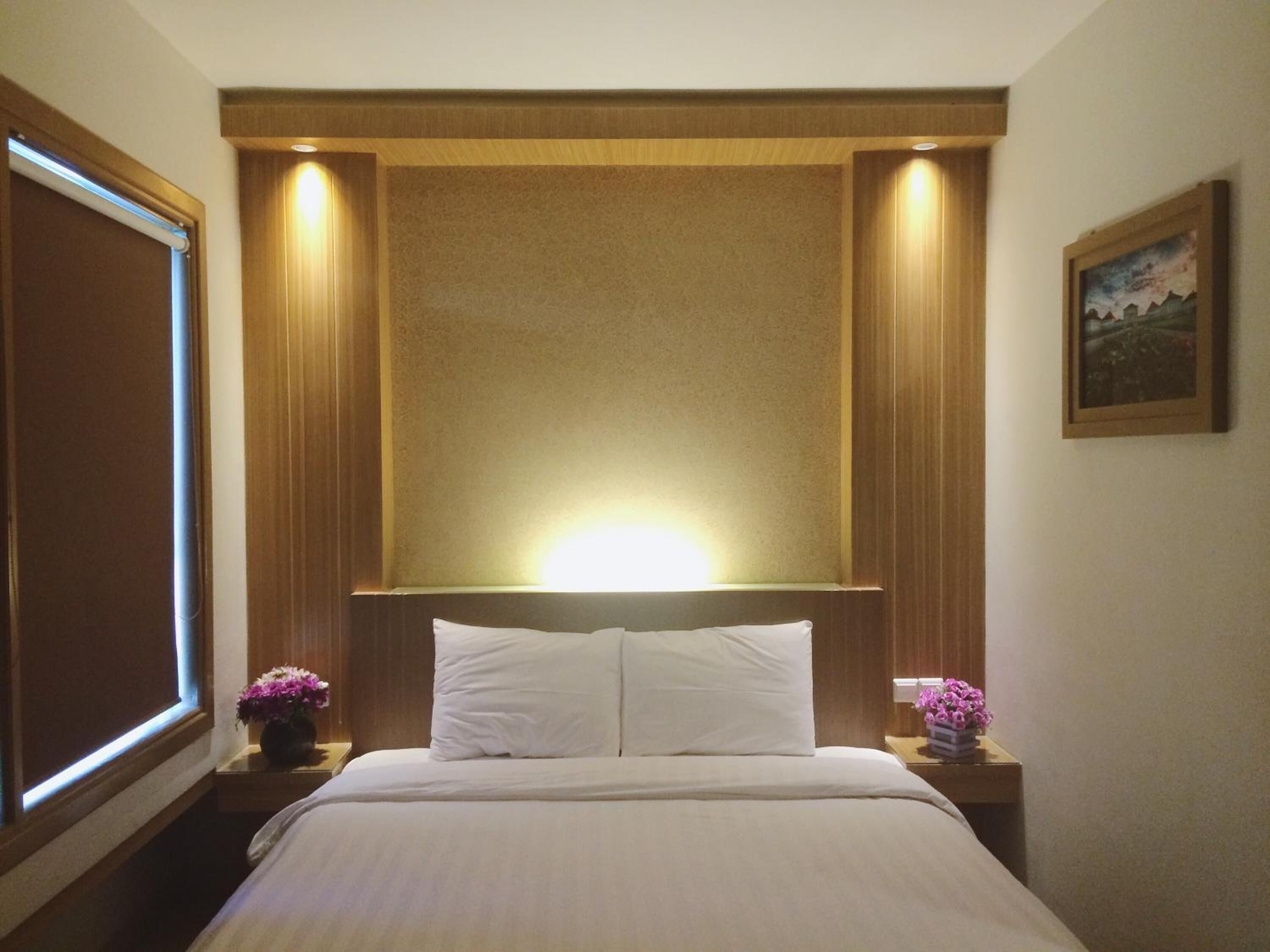 Habitació d'hotel amb un llit gran, un capçal de llit de fusta i dues taules de nit amb bocs de flors.