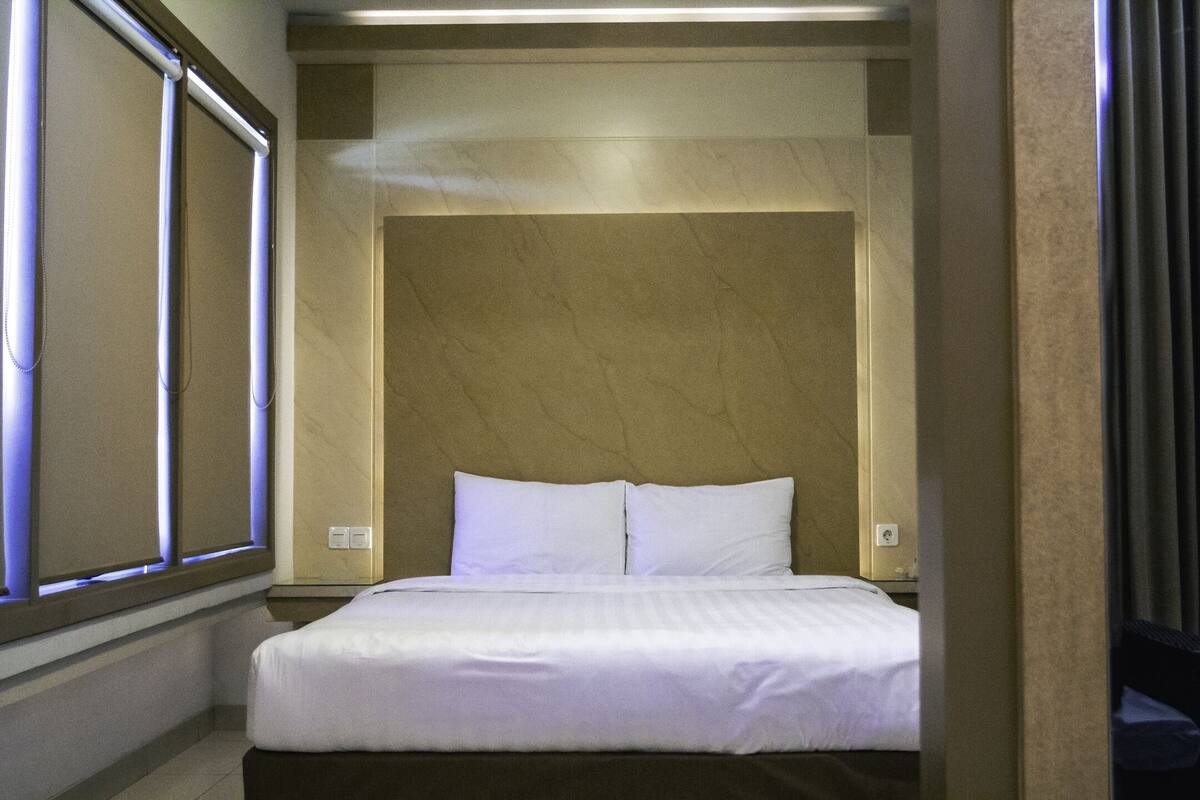 Una habitación de hotel con una cama, un cabecero y una ventana con persianas.