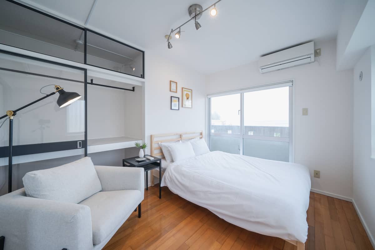 A modern bedroom with a bed, a desk, a chair, and a window.