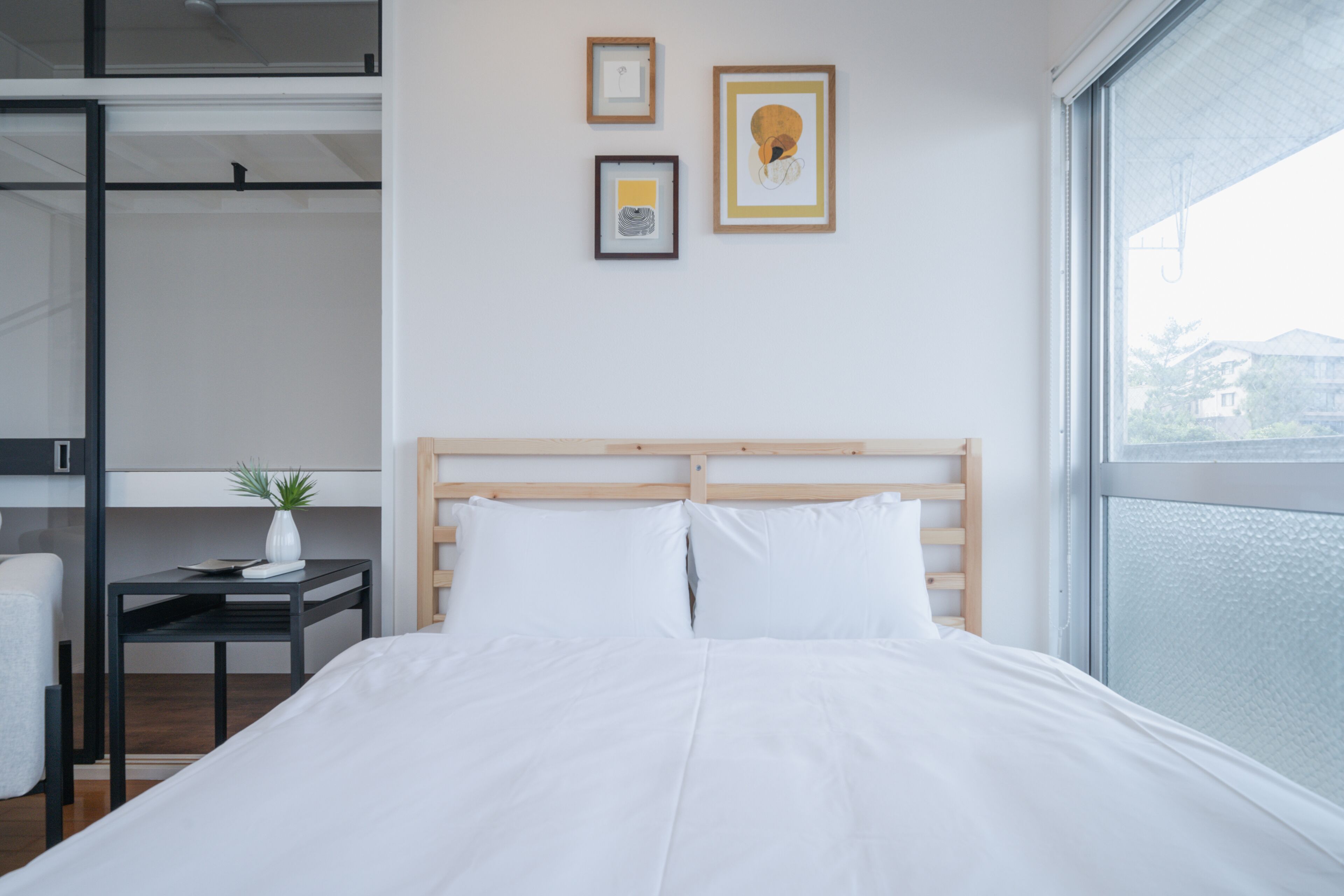 A modern hotel room with a large bed, a small table with a plant, and artwork on the wall.