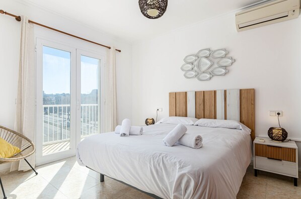 A hotel room with a large bed, a chair, a nightstand, and a wall-mounted light fixture.
