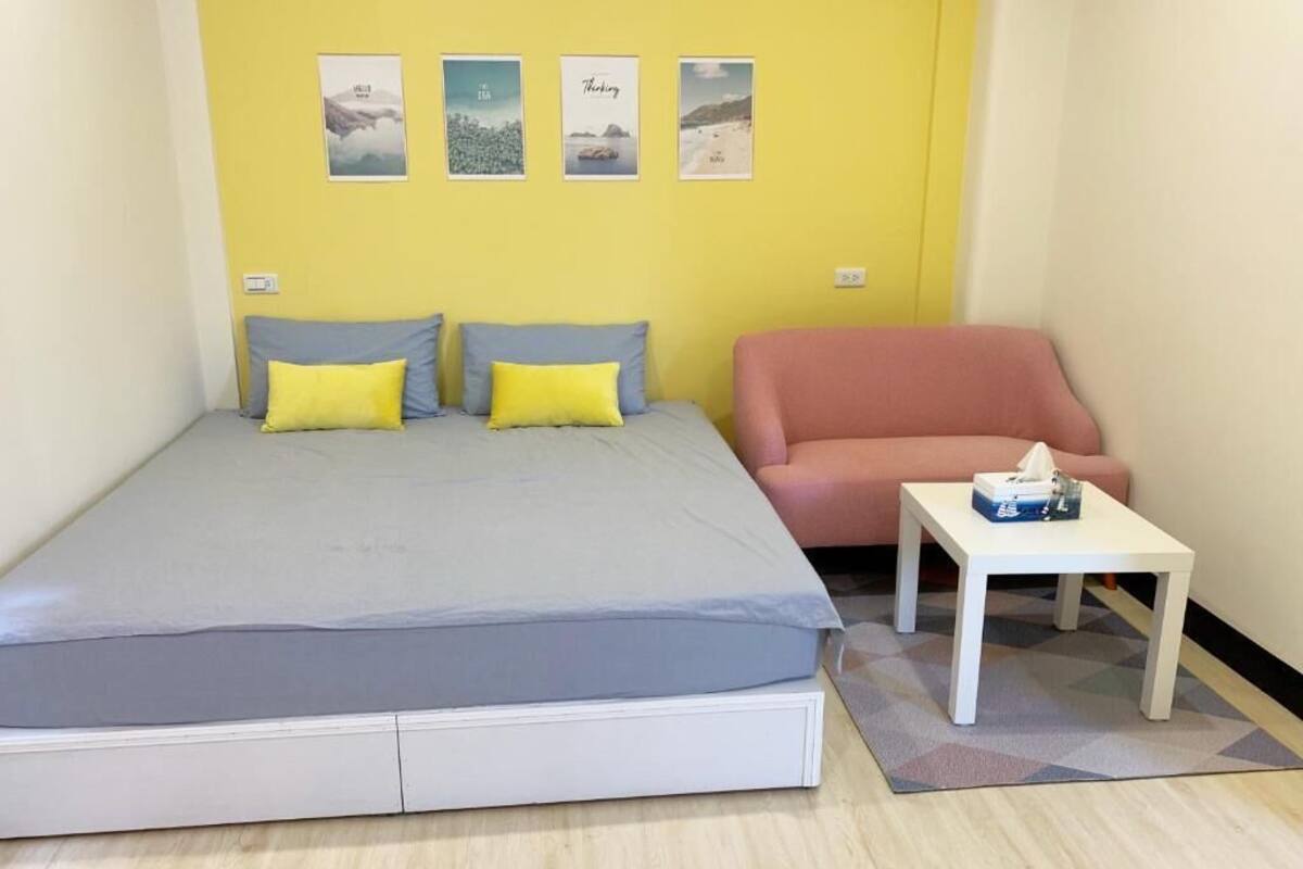 A bedroom with a bed, a chair, a small table, and four framed pictures on the wall.