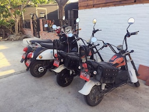 Tres scooters estacionados uno tras otro frente a una pared blanca.