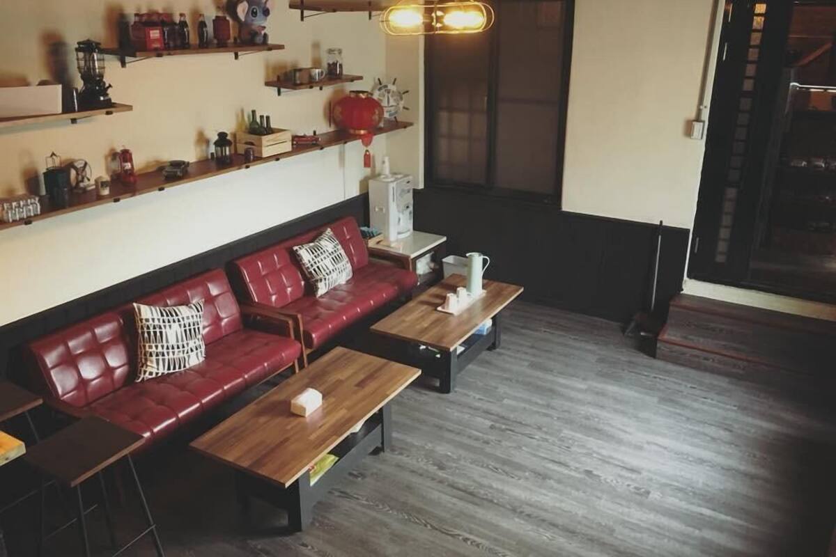 A cozy living room with a red leather sofa, wooden coffee table, and shelves with various items.