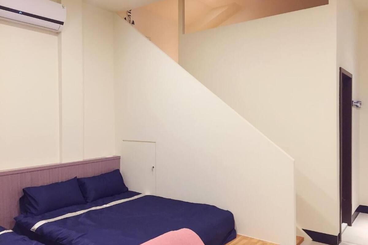 A bedroom with a bed, a wooden bench, a white door, and a staircase.