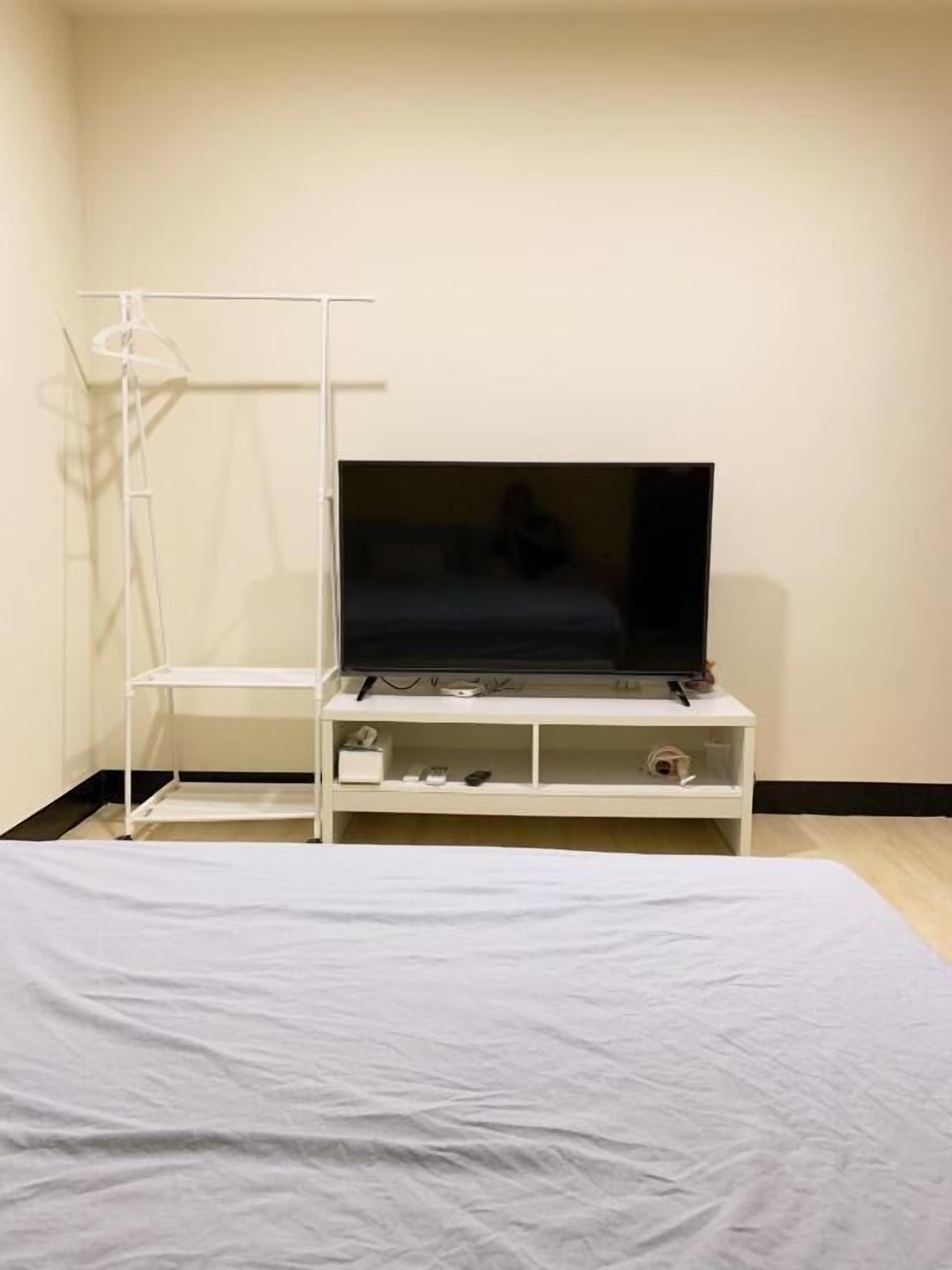 A bedroom with a bed, a TV on a white stand, and a white wardrobe.