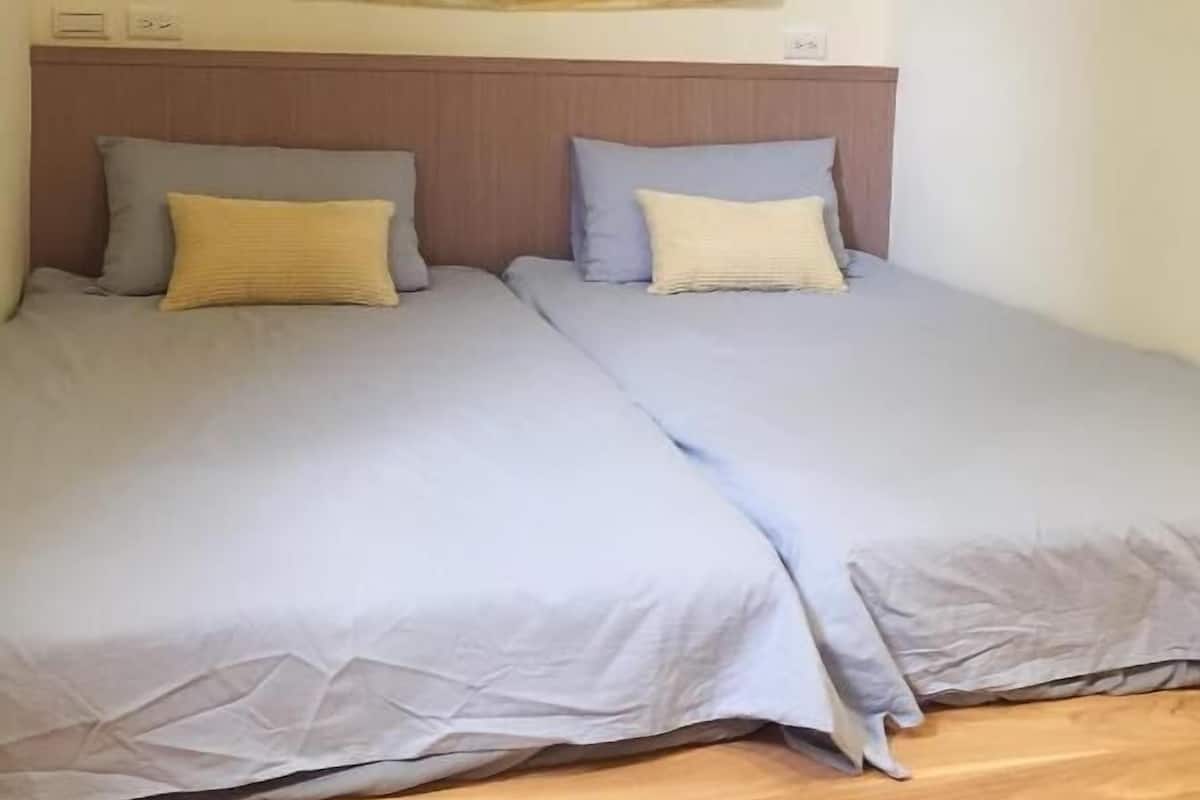A room with two beds, a wooden headboard, and a large window with curtains.