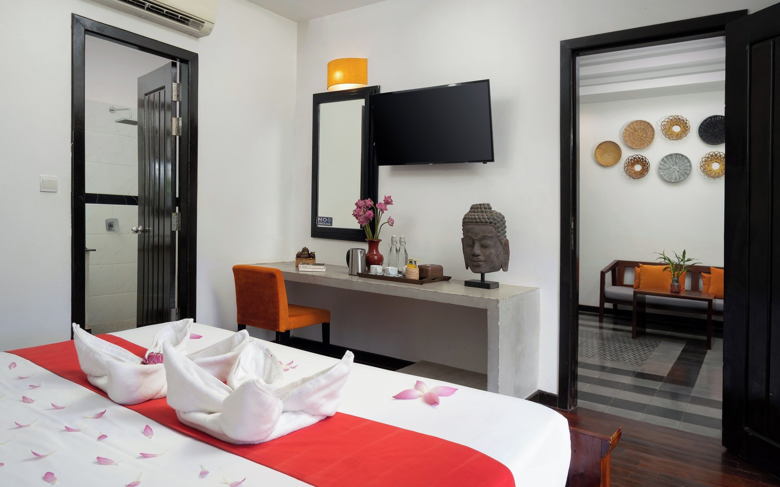 A hotel room with a bed, a desk, a chair, a TV, and a Buddha statue.
