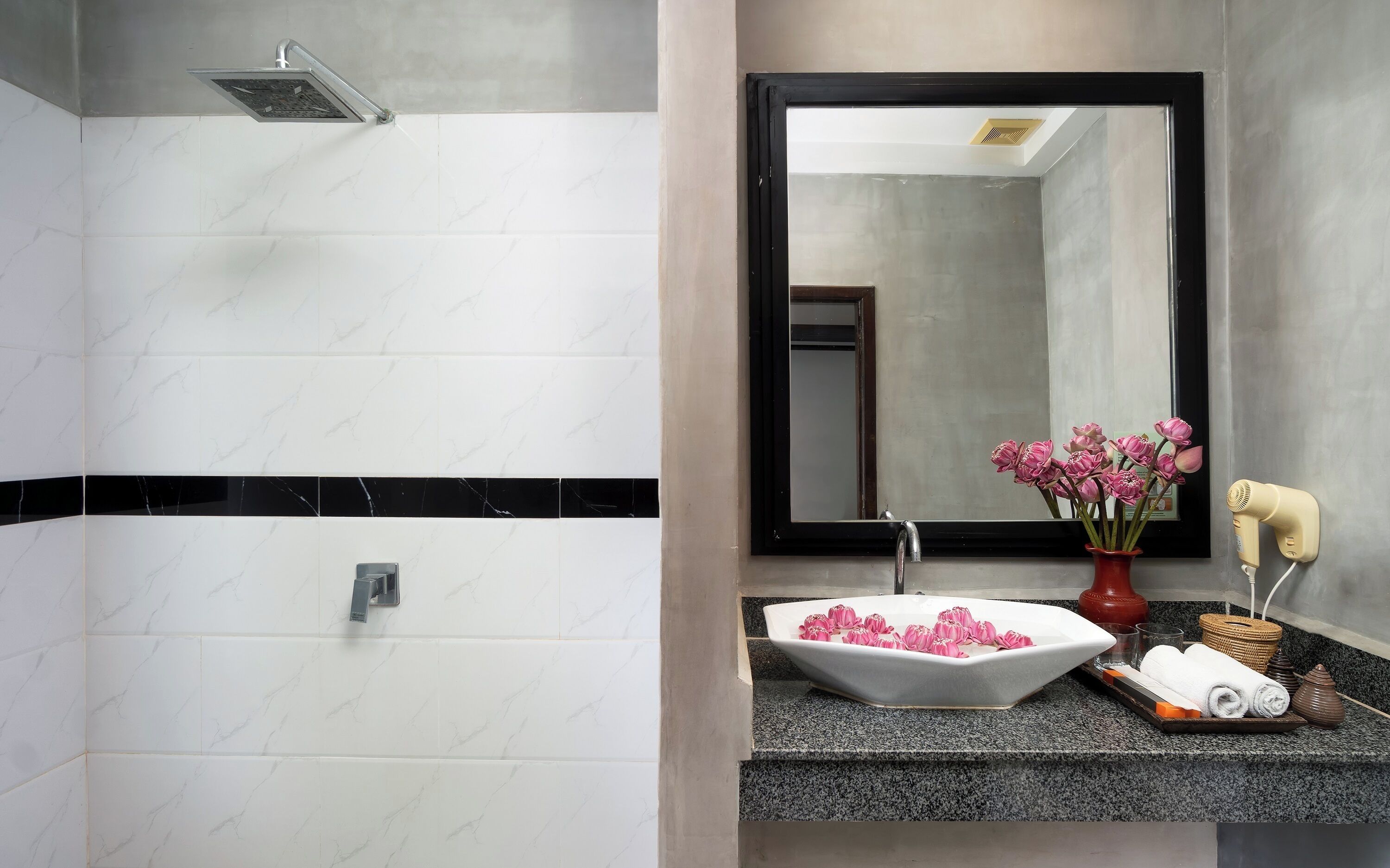 Un baño con ducha, lavabo, espejo y un florero con flores.