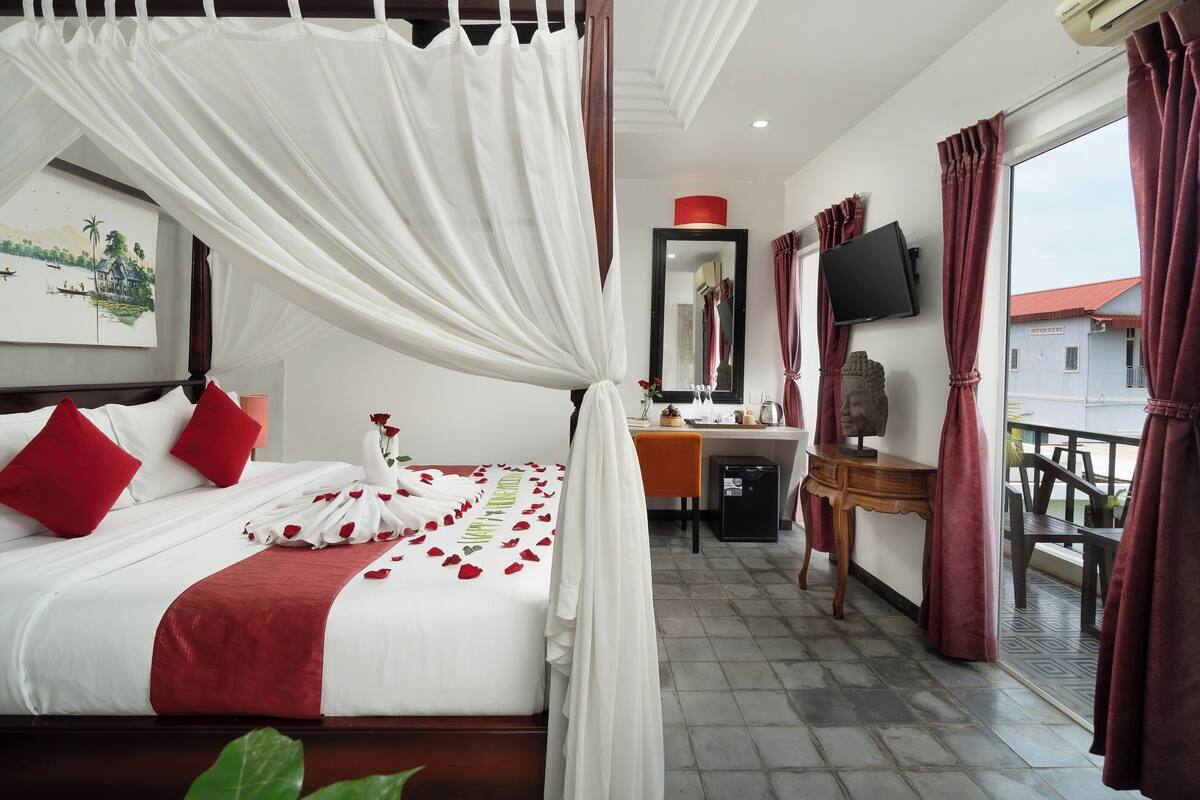 Una habitación de hotel con cama, escritorio, televisor y balcón.