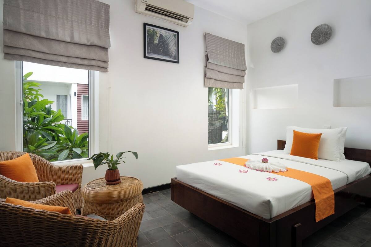 Habitación de hotel con cama, una silla, una mesita con una planta y una ventana con vistas a zonas verdes.