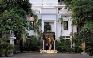 Ein Gebäude mit weißer Fassade, umgeben von üppiger Vegetation und einem Eingang mit Stufen.