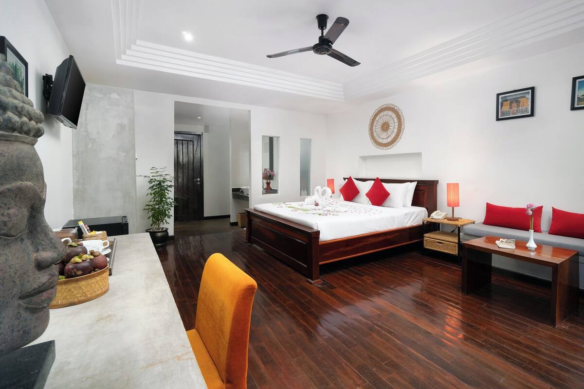 Habitación de hotel con cama, sofá, escritorio, silla, ventilador de techo y planta en maceta.