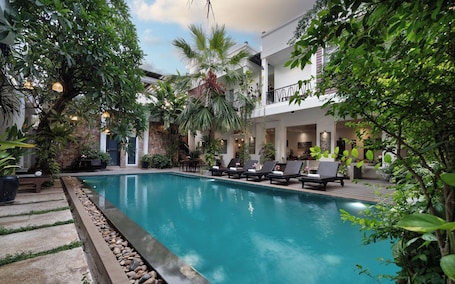 A pool area with lounge chairs, a stone wall, and lush greenery.. Boutique Indochine d'Angkor
