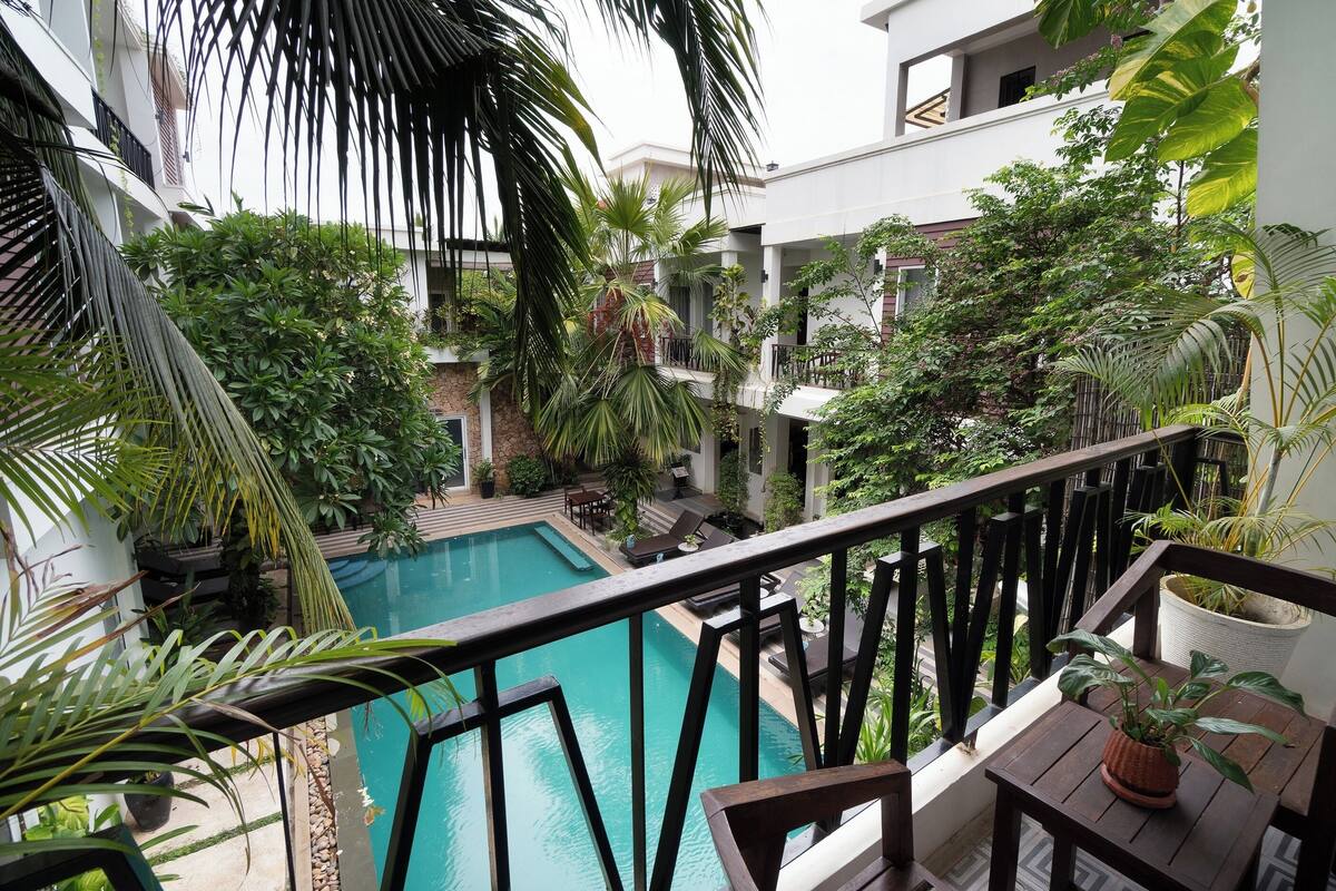 Una piscina rodeada de exuberante vegetación, una terraza de madera y un muro de piedra.