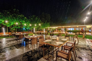 An outdoor restaurant with tables and chairs arranged under a covered area, surrounded by greenery. - Go Green Spice Eco Resort (Cavelossim)
