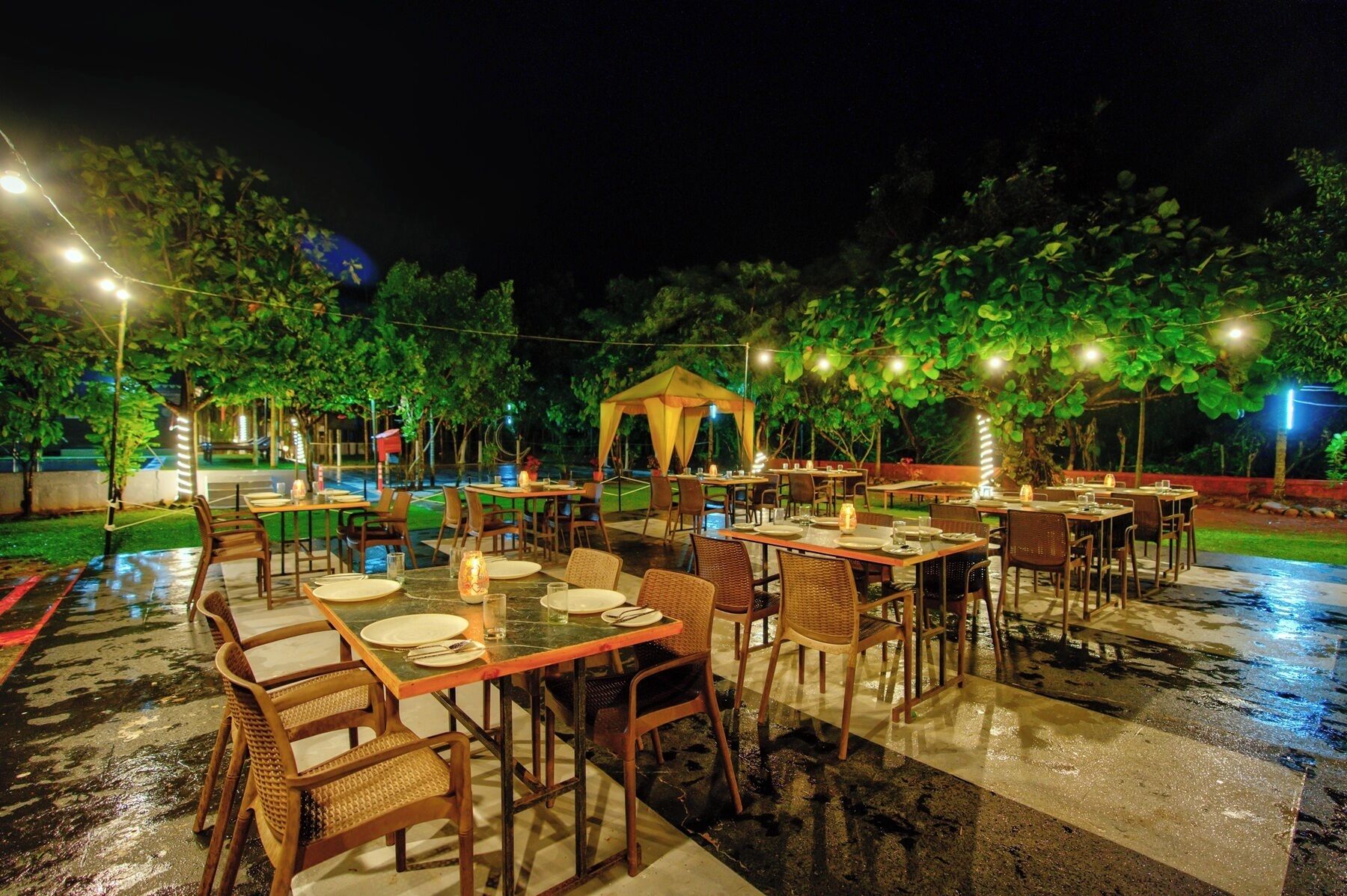 An outdoor dining area with tables and chairs, a covered seating area, and string lights.