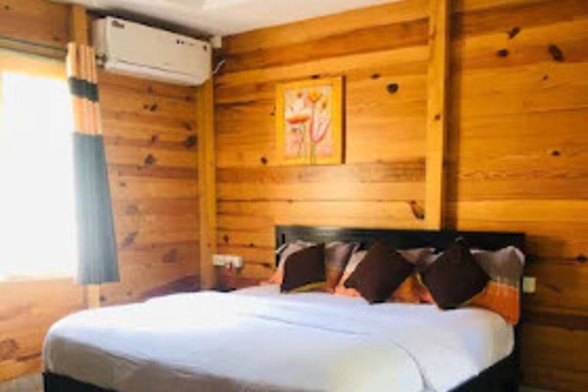 A wooden-paneled room with a bed, a small table, and a window with curtains.