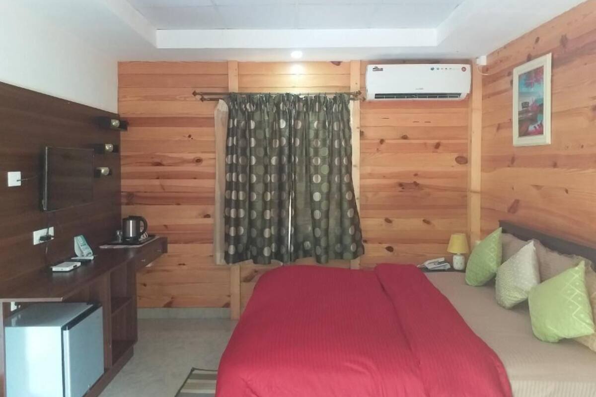 A room with a bed, a small desk, a TV, an air conditioner, and a curtain.