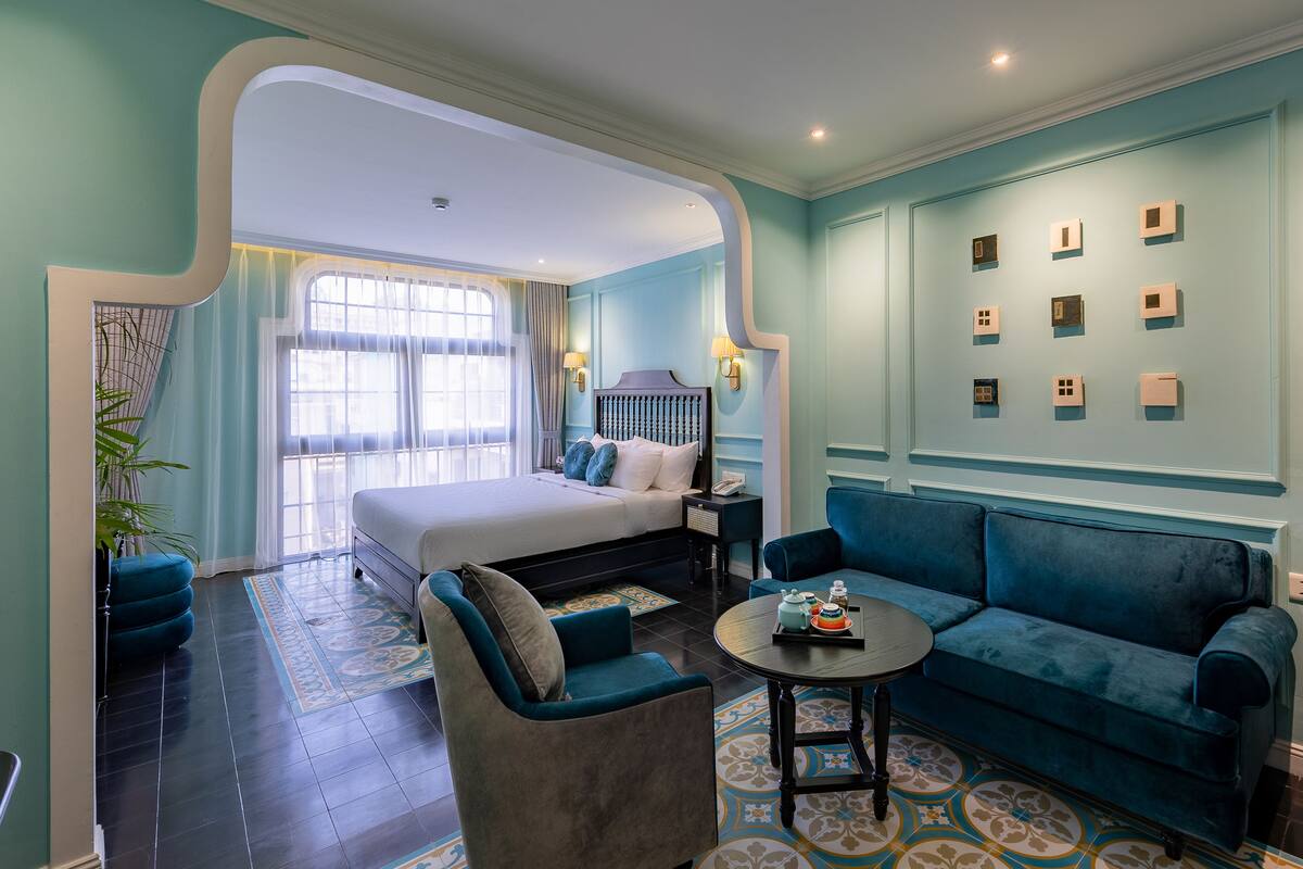 A modern hotel room with a bed, a sofa, a small table, and a wall with decorative elements.