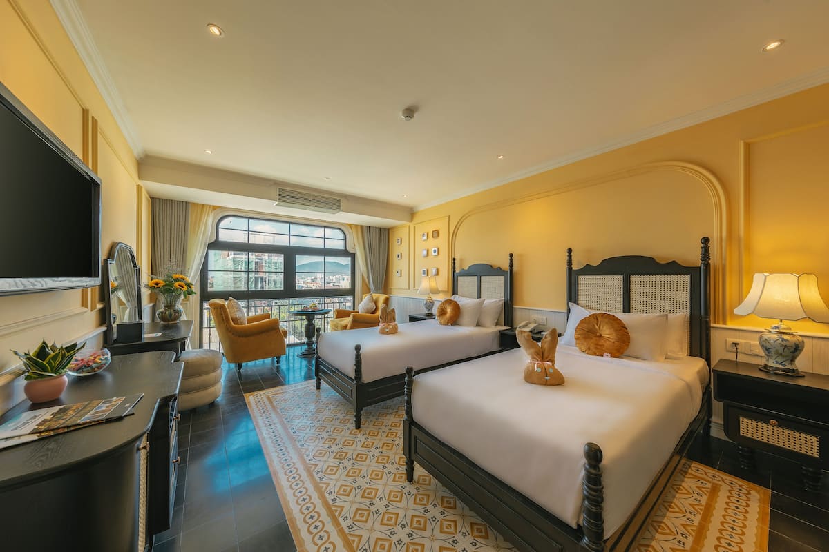 A hotel room with two beds, a desk, a chair, a TV, and a large window.