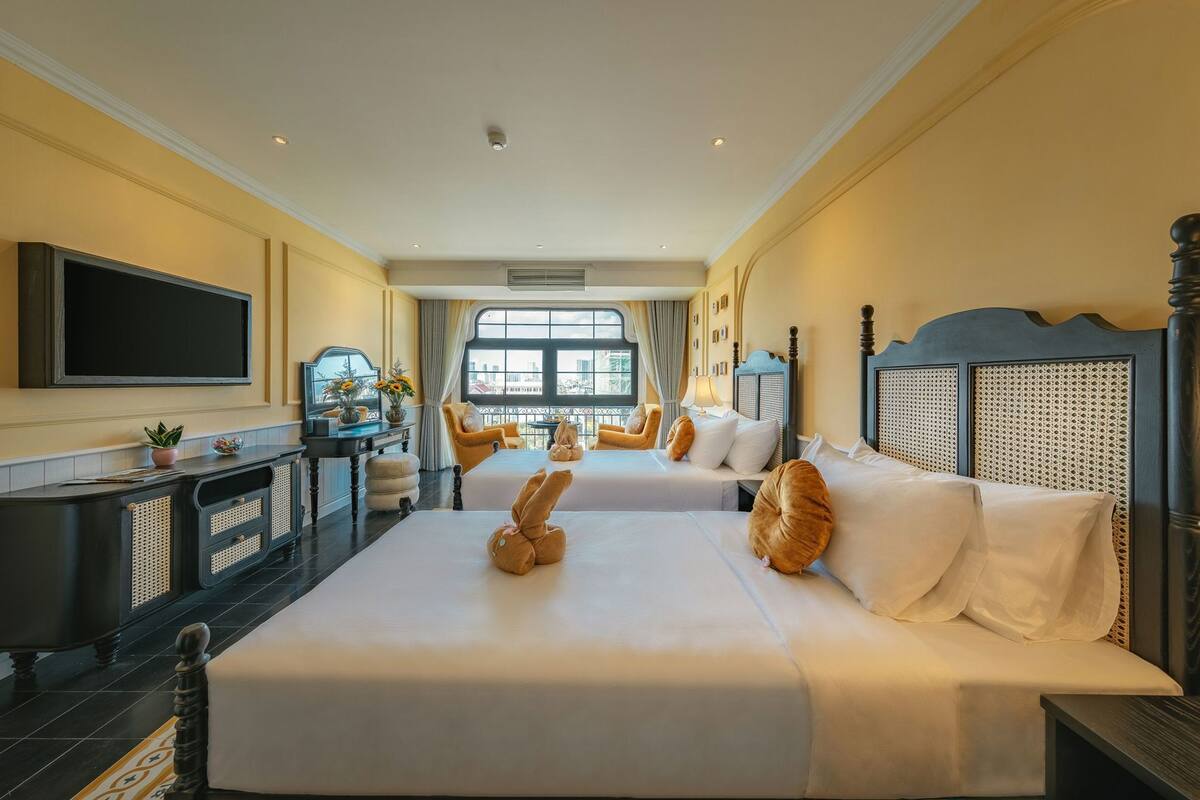A hotel room with two beds, a TV, a desk, and a large window.