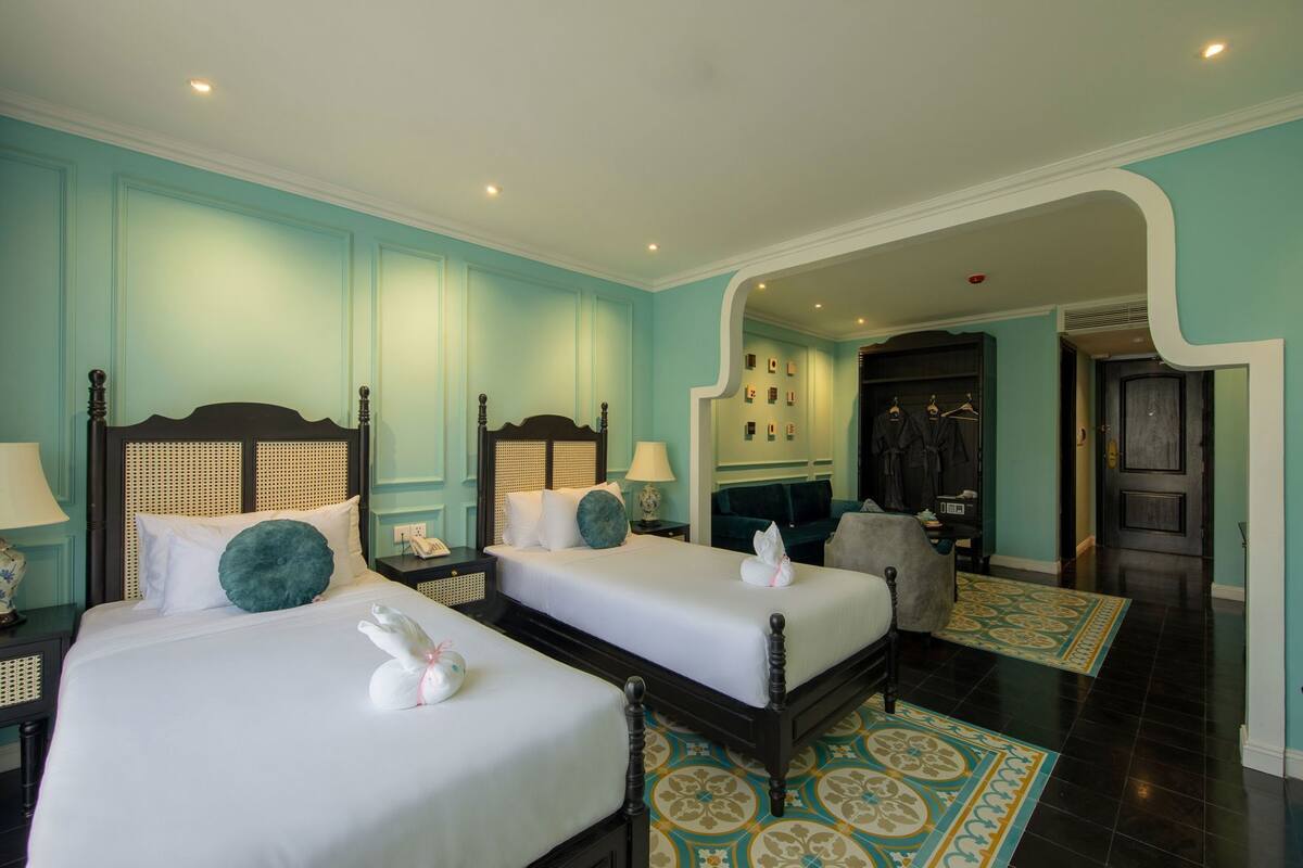 A hotel room with two beds, a sitting area, and a bathroom visible through an archway.